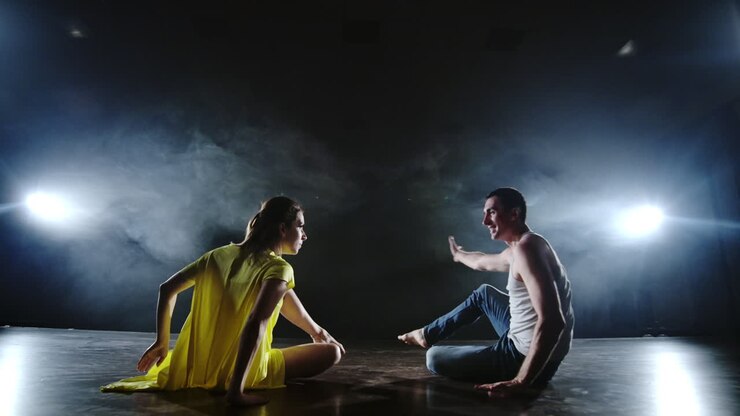 Zoom della telecamera. Coreografia romantica moderna. L'amore è in scena. Un uomo e una donna ballano insieme una danza divertente in jeans e un vestito giallo sul palco nel fumo. Musical.