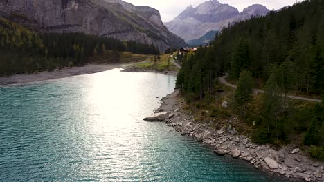 aerial view of mountains, fall forest and sun reflection at turquoise glacier lake oeschinensee