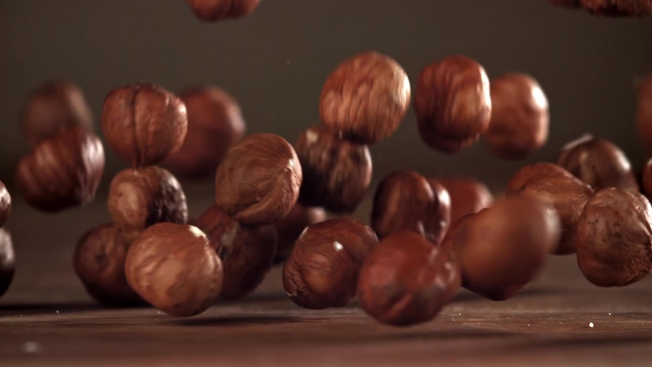 Nocciole sgusciate che cadono al rallentatore su un tavolo di legno