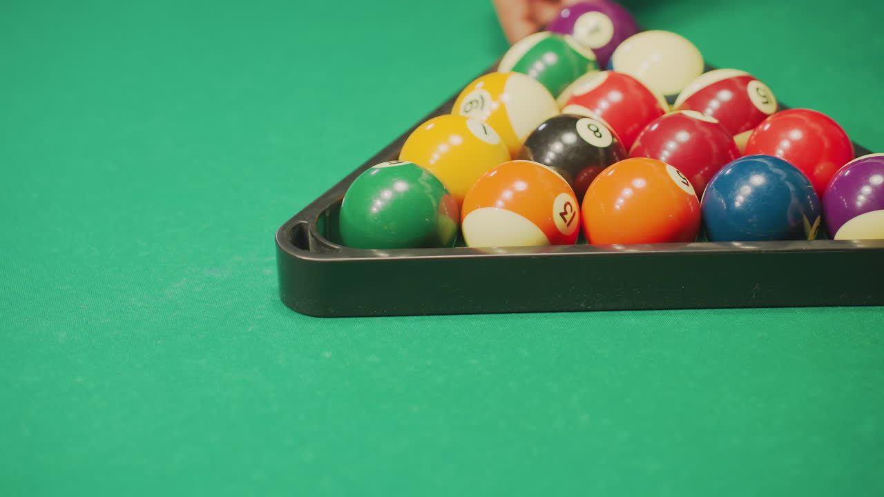 Close-up of hand rolling a well-arranged set of colorful billiard balls in triangle formation on green pool table. The vibrant balls are precisely aligned, capturing a moment of focus and preparation
