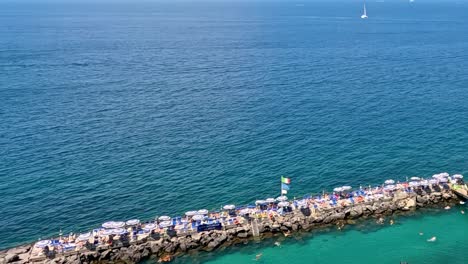 Aerial footage showcasing a breakwater with sunbathers and expansive views of the open sea.