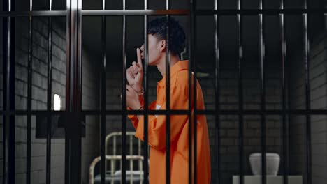 vista lateral de un prisionero masculino asiático con esposas haciendo un gesto de silencio mientras está de pie en la cárcel