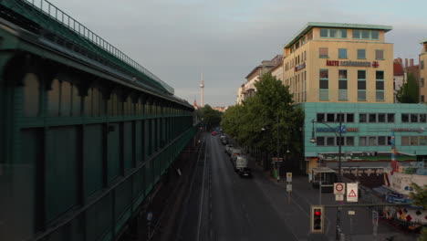 Forwards-fly-around-elevated-Ubahn-station-at-Schoenhauser-Allee-street.-Ascending-footage-reveals-cityscape-with-Fernsehturm-TV-tower.-Berlin,-Germany