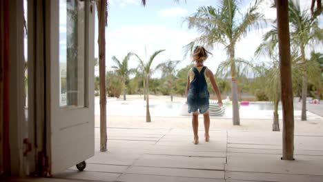 caucasian girl running and raising hands at swimming pool at beach house with palm trees