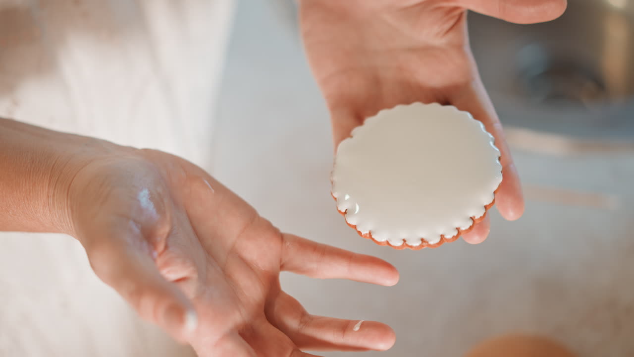Hands with cookie. Close image of hands grasping frosty pumpkin treat in cozy kitchen. Detailed shot capturing hands softly handling chilled pumpkin cookie amidst flour and gentle light