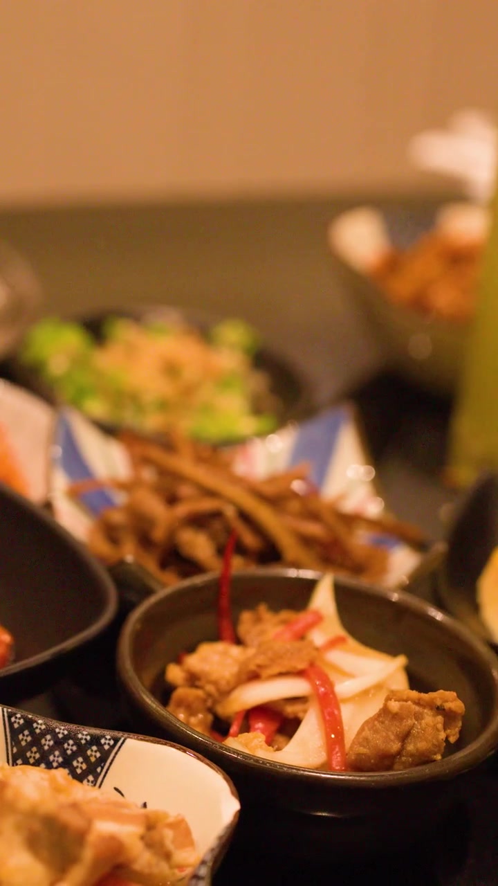 Close-up of hand arranging various small plates of Japanese cuisine on dark restaurant table.