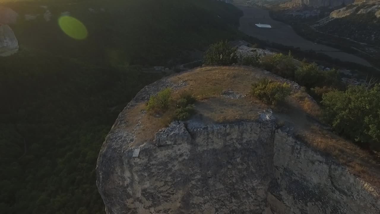 Aerial view of a mountain cliff with a valley and river below at sunrise/sunset.