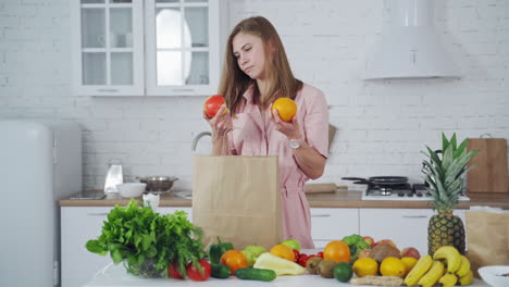 pretty woman takes fresh fruit from paper bag. young model is sniffing organic fruit on the light kitchen background. many healthy food on a table for losing weight. vertical video