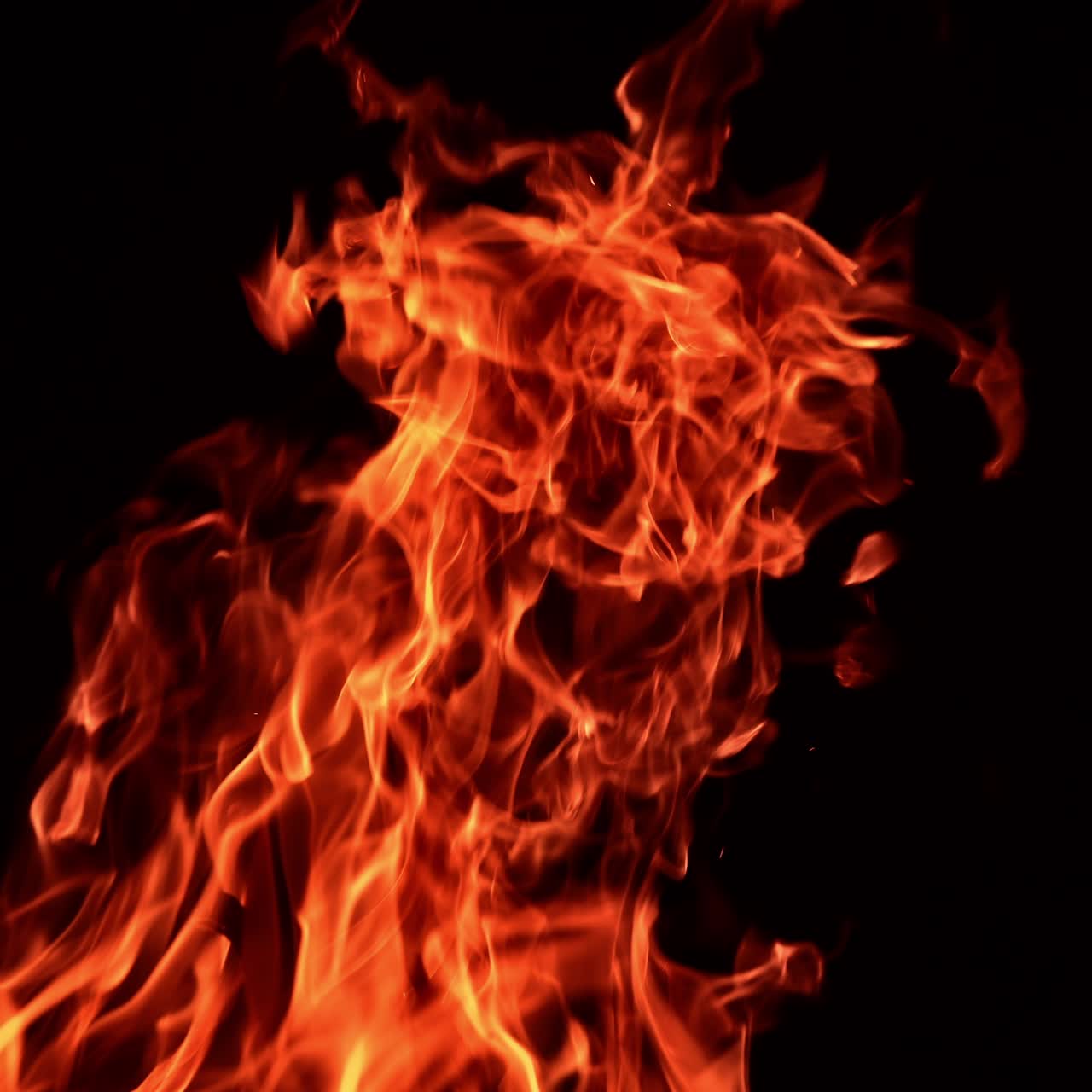 Fiamme arancioni vive di un falò che si innalzano nell'aria. Vista ipnotica di un fuoco che brucia su uno sfondo nero.