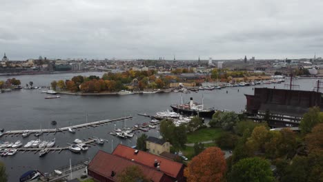 Vista-Aérea-Alejándose-Del-Museo-Vasa-En-Estocolmo,-Suecia,-Se-Puede-Ver-La-Isla-Djurgarden,-Al-Fondo-La-Ciudad-Con-Sus-Canales