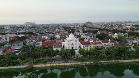 Un-Dron-Rodea-La-Mezquita-Ramlie-Musofa-Mientras-El-Tráfico-Pasa-Por-El-Lago-Sunter-En-El-Norte-De-Yakarta,-Indonesia