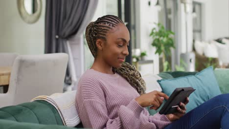 Happy-african-american-woman-using-tablet-and-sitting-on-sofa