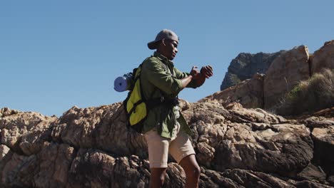 african american man hiking in countryside by the coast using his smartwatch