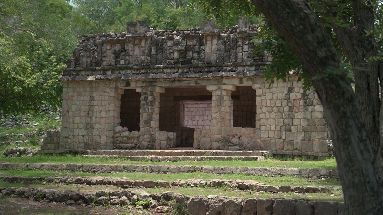 Inquadratura fissa e ampia di un antico edificio Maya in pietra con colonne incorniciate da alberi della foresta nel sito archeologico di Labna nello Yucatan, Messico.