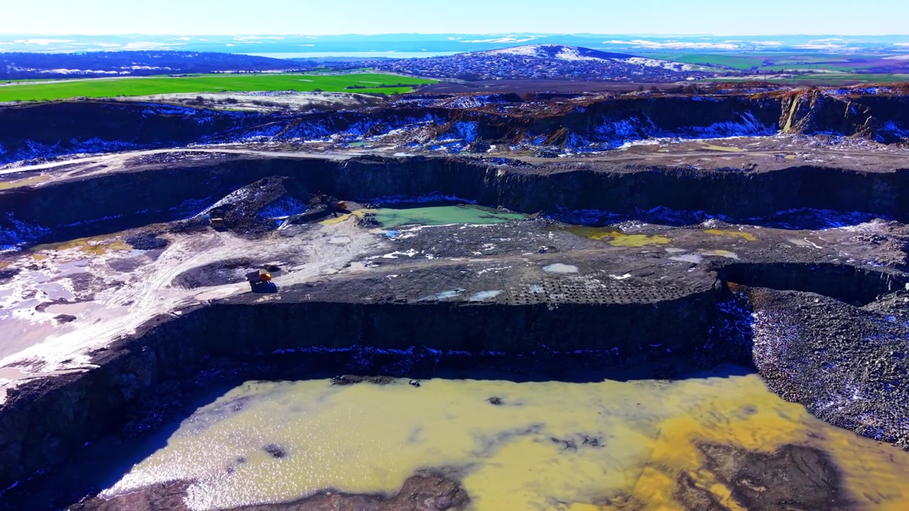 Panoramic view of quarry pit with mineral colored ponds. Green, yellow and orange water pools amid rock terraces and hills.