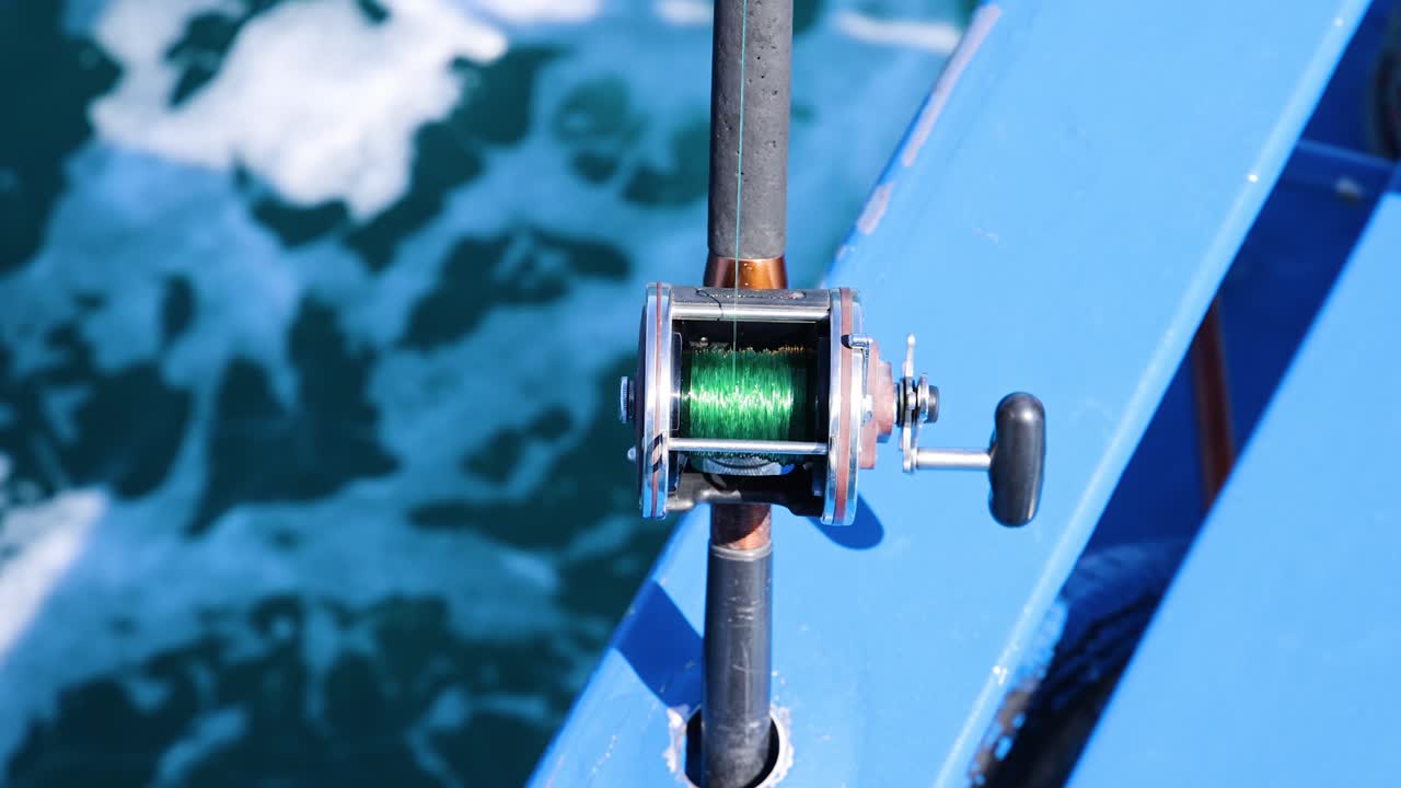 A fishing rod is mounted on a boat, with the ocean waves visible below, captured in bright daylight