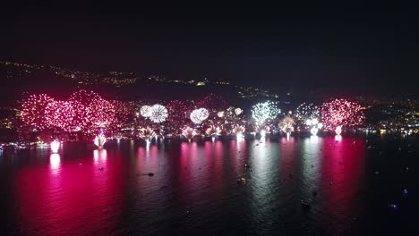 fireworks lighting up city by the sea coast, colorful light reflection on sea water, new year celebration, static aerial drone view, night