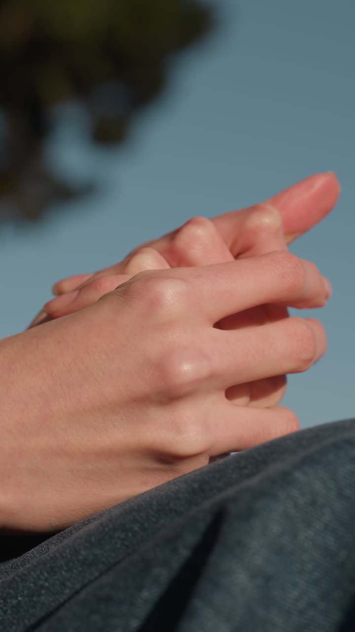 한 사람의 손이 서로 는 클로즈업, 깊은 상이나 생각을 암시합니다. 그 사람의 얼굴은 보이지 않으며, 파란 청바지와 갈색 코트만 볼 수 있습니다.