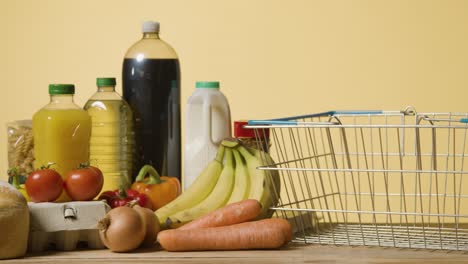 studio shot of basic food items next to supermarket wire shopping basket 2