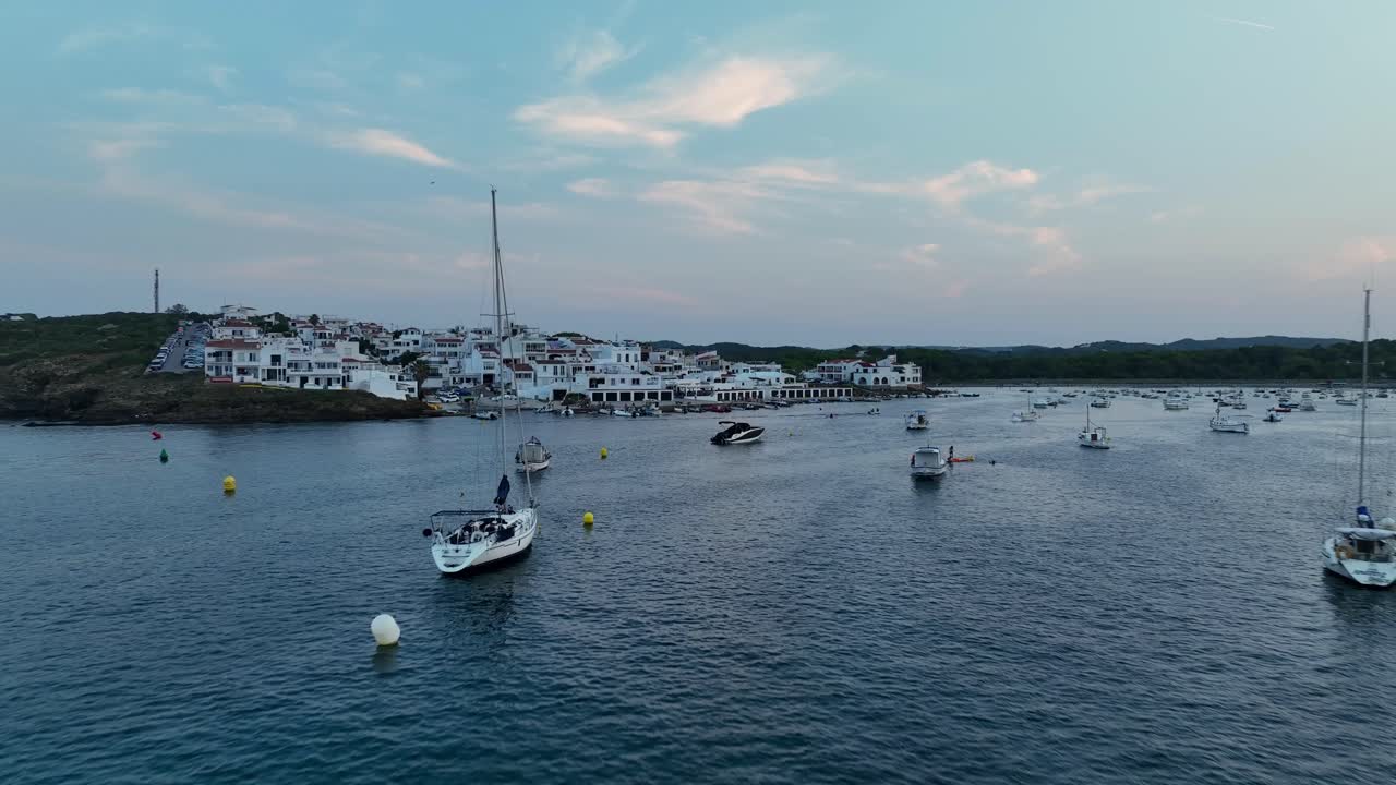 A drone shot flying low by the water and some anchored boats, then rising and filming a village.