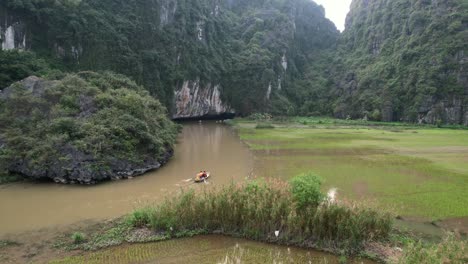 tourists on sampan boats travel on ngo dong river entering grotto or cave at limestone gorge in ninh binh vietnam, sunset - revealing aerial view