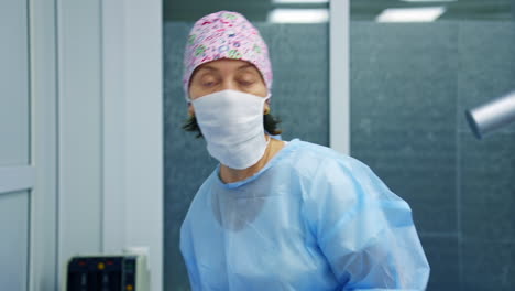 professional ophthalmologist discusses surgery operation to the camera. woman medic in scrubs and mask stands on modern equipment background.