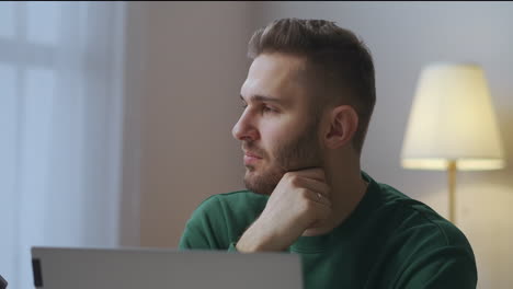 thoughtful man is sitting in front screen of laptop working writer or journalist writing at home at evening portrait shot indoors