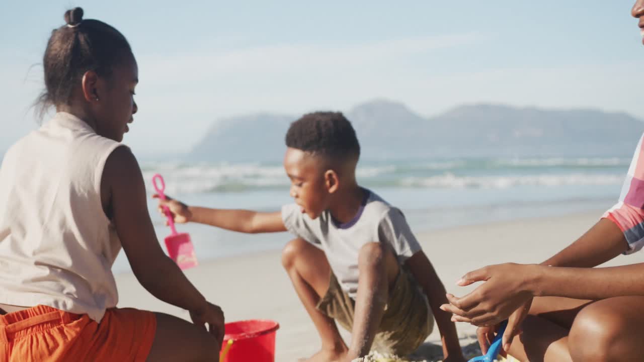 African american mother, daughter and son playing in the sand on the beach