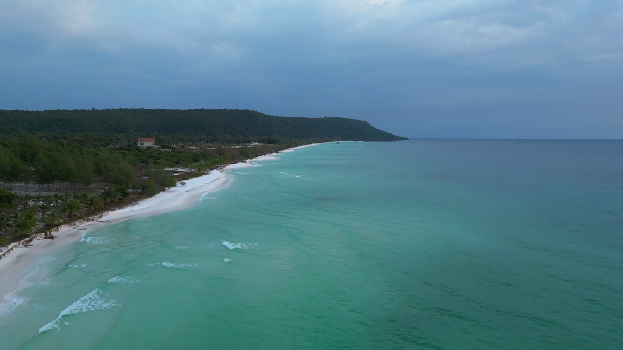 Turquoise waves crashing on the white sandy Sok San Beach in Koh Rong island, Cambodia, at sunset. Great aerial view flight drone shot footage from above
