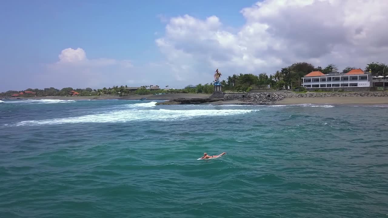Surfer in the ocean near a statue on a beach in Bali