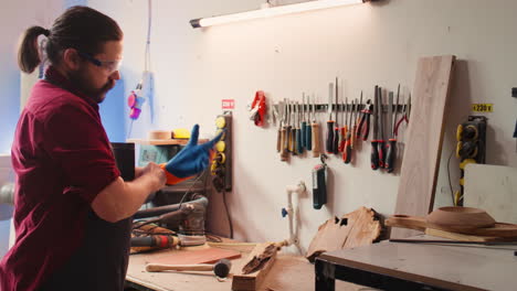 carpintero en un taller de carpintería que se pone guantes de protección