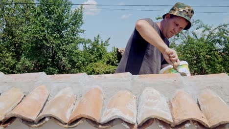 Builder,-cigarette-in-mouth-repairs-terracotta-tiled-wall-with-cement