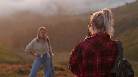 woman taking a picture of a friend on a mountaintop at sunset