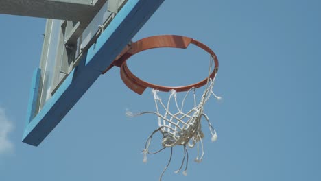 torn net on an outdoor basketball hoop moves in the wind