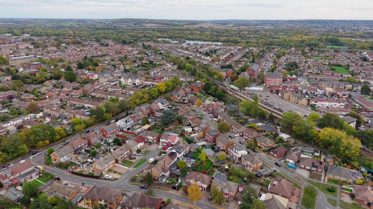 Aerial drone flies over Waltham Cross, heading towards Lea Valley. Roads lined with trees, houses, and Theobalds Grove train station are visible, capturing suburban streets and surrounding greenery
