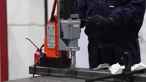 metal worker drilling at a factory wearing blue protective suit