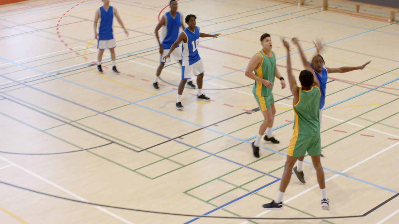 Multiracial male basketball players in gym with male coach walking and observing game