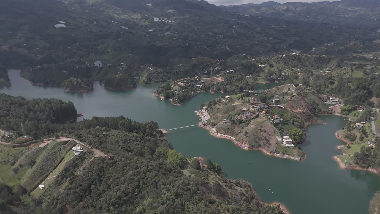 A stunning aerial view of the Guatapé Reservoir in Antioquia, Colombia. The emerald-green waters wind through lush, mountainous terrain, creating a patchwork of peninsulas and islands