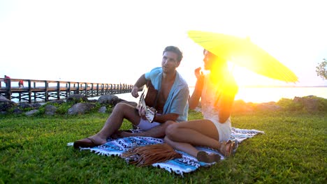 multi ethnic couple enjoying beach picnic playing guitar