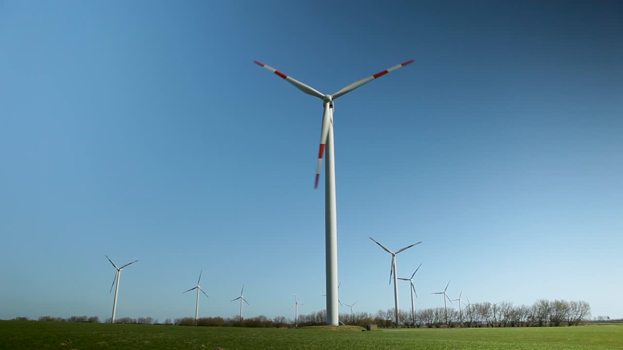 Wind turbines stand tall under a clear blue sky in a serene grassy field, generating renewable energy