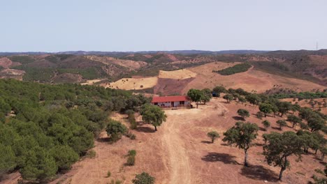 Antena-De-Una-Casa-De-Campo-Solitaria-En-Medio-De-Vastas-Tierras-De-Cultivo-En-Montañas-Inclinadas-De-Alentejo,-Portugal