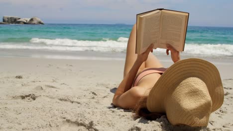 mujer caucásica con sombrero leyendo un libro en la playa 4k