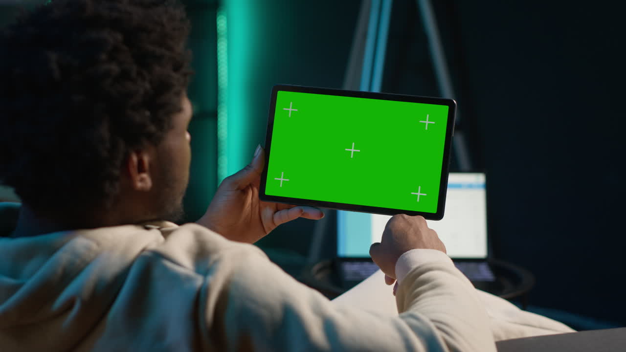 African american freelancer uses copy space display on tablet to work from the comfort of his home, sitting on the couch in his trendy stylish living room. Happy young adult on web. Camera A.