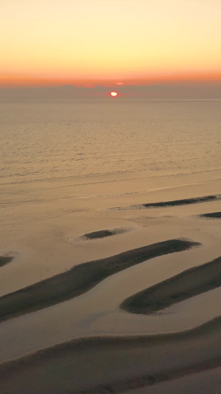 Wertykalny kadr drona przedstawiający wschód słońca nad spokojną zatoką, blask słońca na wodzie i gładki horyzont z delikatnymi chmurami. Pejzaż morski w wysokiej rozdzielczości, z spokojnym nastrojem i otwartą przestrzenią.