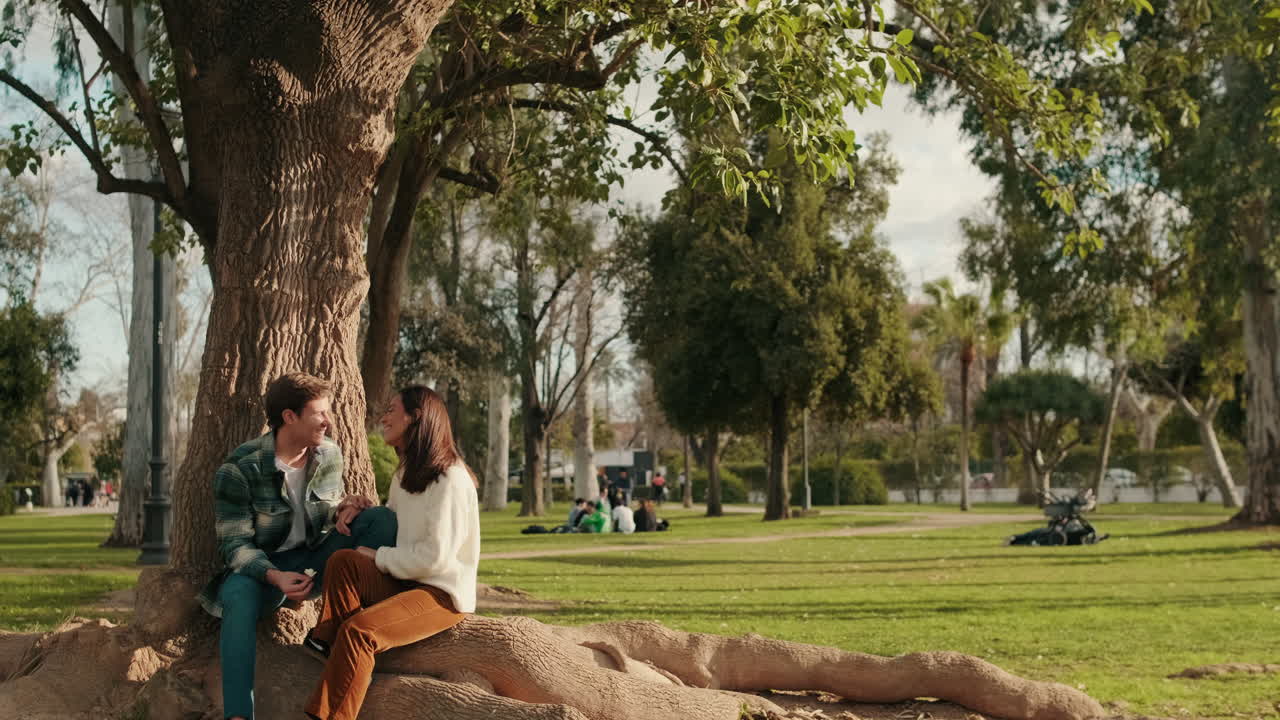 Happy young couple man and woman talking and laughing sitting in the park under