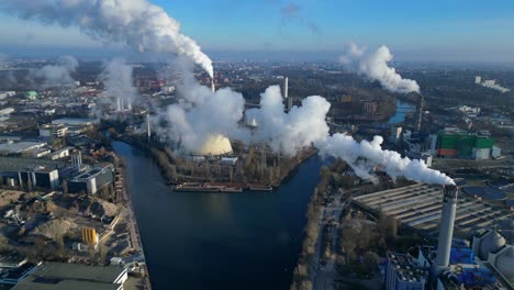 aerial view of a thermal power plant emitting smoke on a sunny day, with a river and a city in the background. stunning aerial view flight drone top down above view