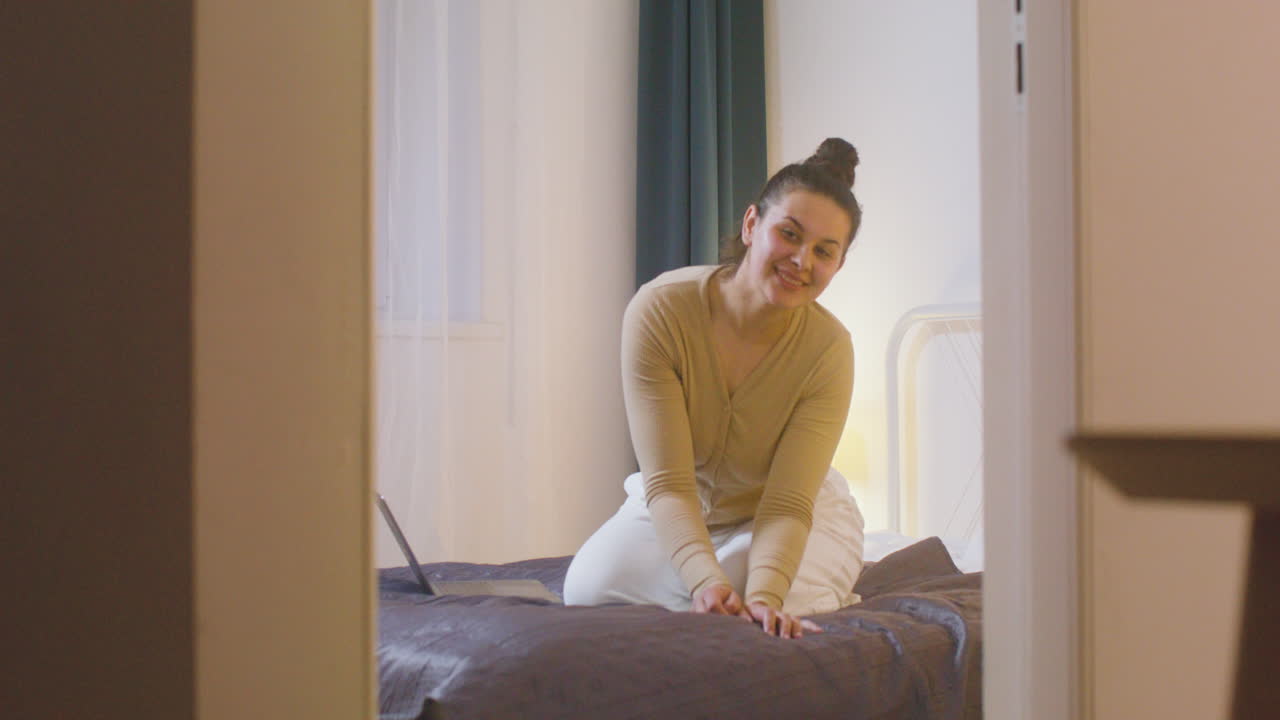 집에서 침대에 앉아 웃는 어머니를 향해 걸어가는 아기의 뒷모습