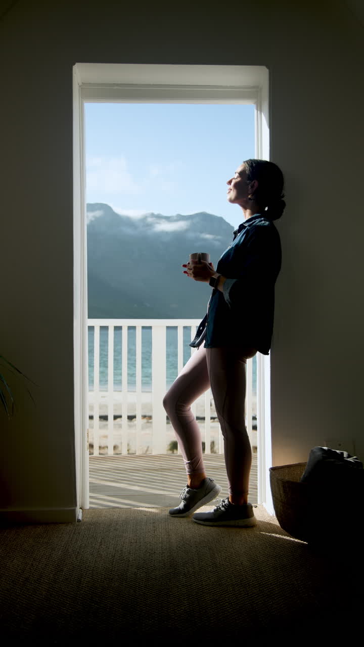 Vertical video: Woman enjoying morning coffee on balcony overlooking scenic mountain view