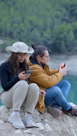 couple relaxing by a lake, enjoying snacks and using their phone during an outdoor break