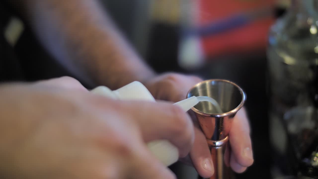 Versare sciroppo in un misurino di metallo mentre si prepara un cocktail, primo piano